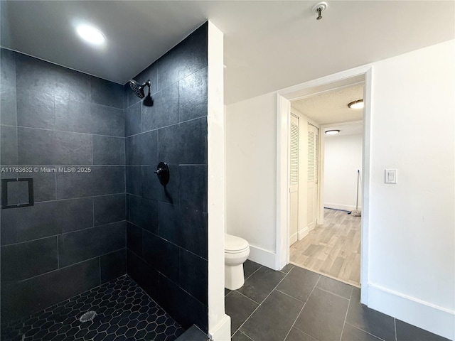 bathroom with baseboards, tiled shower, and toilet