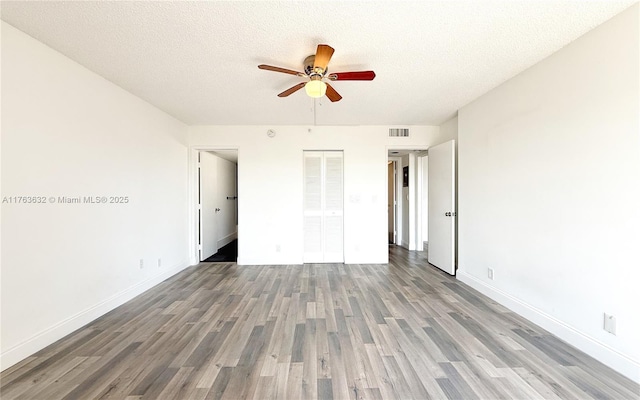 unfurnished bedroom featuring visible vents, baseboards, a textured ceiling, and wood finished floors