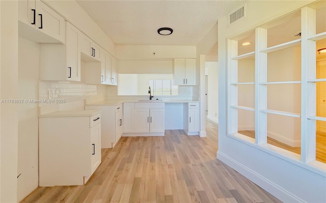 kitchen with light wood-style flooring, visible vents, white cabinets, and a sink