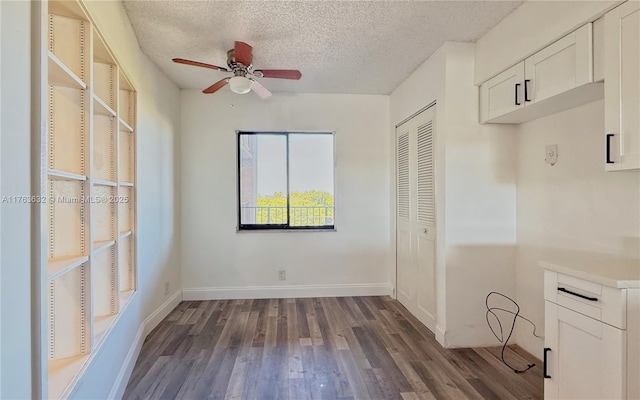 interior space with dark wood-style floors, baseboards, a textured ceiling, and ceiling fan