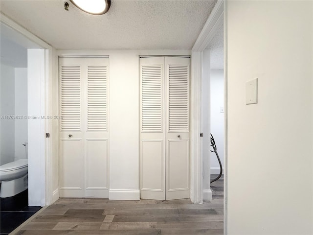 hall with wood finished floors, baseboards, and a textured ceiling