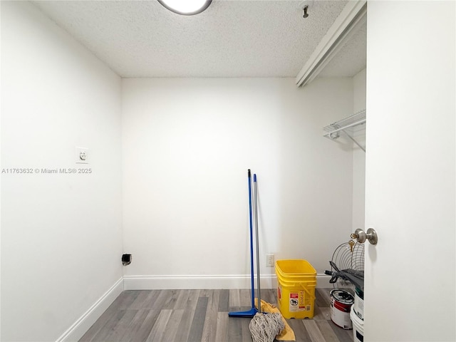 laundry room featuring electric dryer hookup, baseboards, a textured ceiling, and wood finished floors