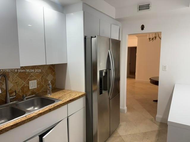 kitchen featuring visible vents, a sink, stainless steel refrigerator with ice dispenser, white cabinetry, and backsplash