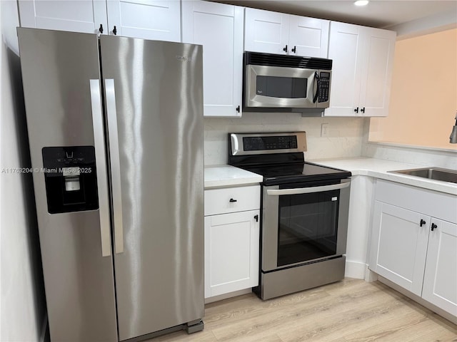 kitchen with recessed lighting, light wood-style flooring, appliances with stainless steel finishes, white cabinetry, and a sink