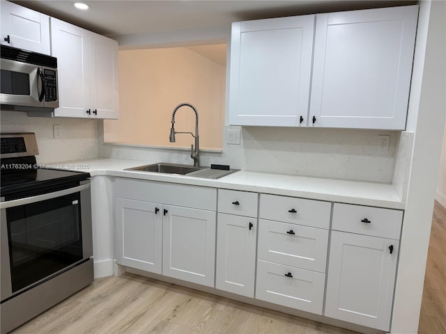 kitchen with a sink, decorative backsplash, stainless steel appliances, white cabinets, and light wood-type flooring