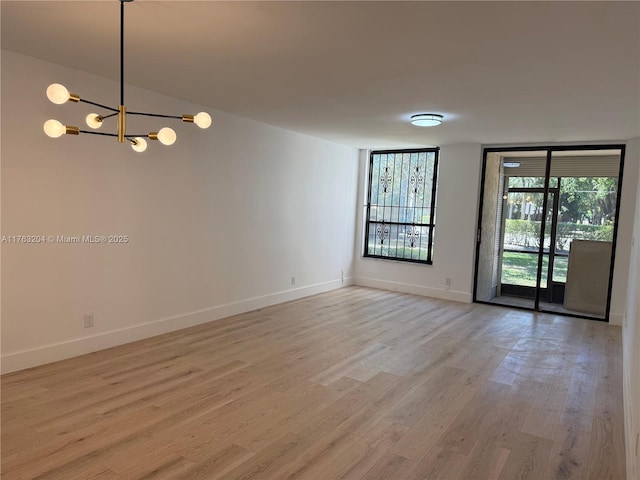 spare room featuring floor to ceiling windows, baseboards, light wood-type flooring, and an inviting chandelier