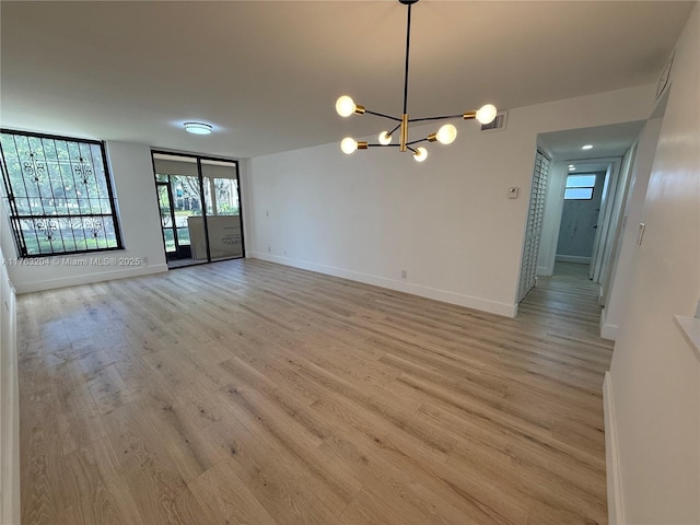 empty room with an inviting chandelier, light wood-style floors, baseboards, and visible vents