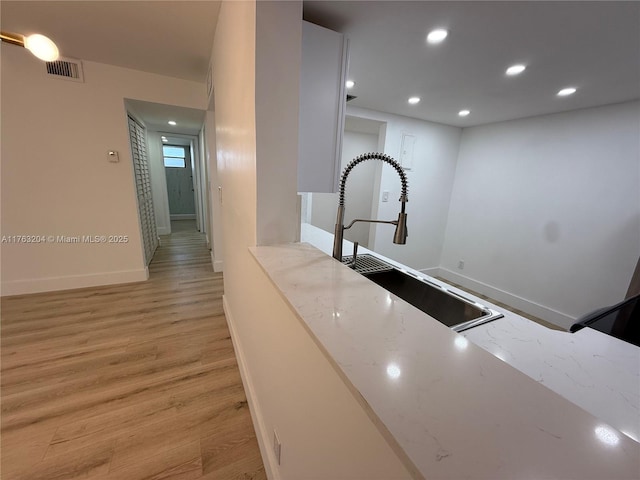 hallway featuring visible vents, a sink, recessed lighting, light wood finished floors, and baseboards