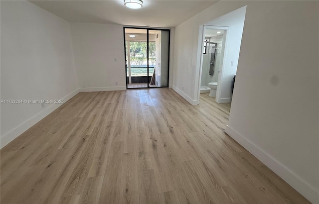 spare room with baseboards, light wood-style floors, and floor to ceiling windows