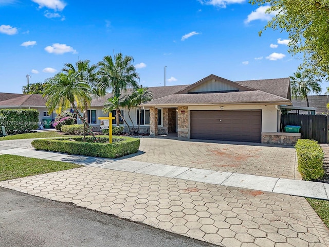 single story home featuring decorative driveway, fence, stone siding, and an attached garage