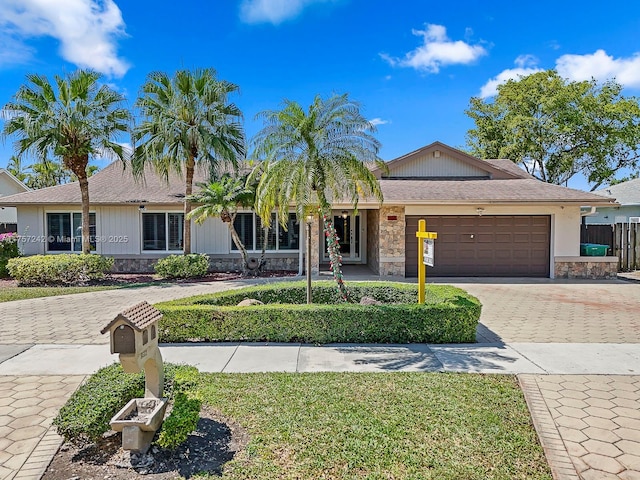 ranch-style house with fence, an attached garage, a front lawn, stone siding, and decorative driveway