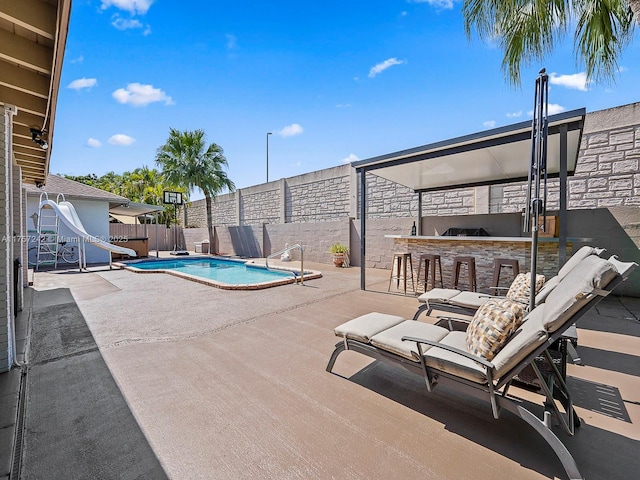 view of swimming pool with a patio area, an outdoor kitchen, a water slide, and a fenced backyard