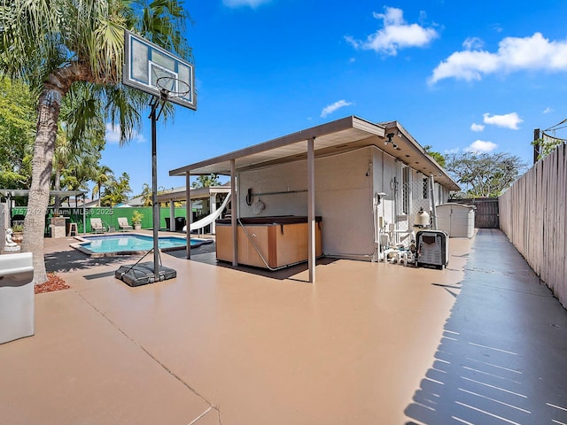 exterior space featuring a hot tub, a water slide, a fenced backyard, a patio area, and a gate