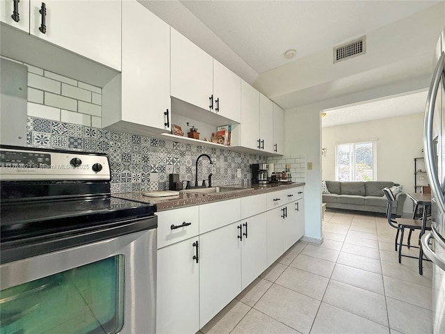 kitchen featuring visible vents, stainless steel electric range oven, decorative backsplash, light tile patterned flooring, and a sink