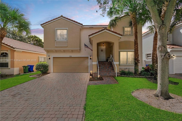 mediterranean / spanish home featuring stucco siding, a tile roof, decorative driveway, a front yard, and an attached garage