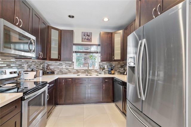 kitchen with dark brown cabinetry, stainless steel appliances, light countertops, and a sink