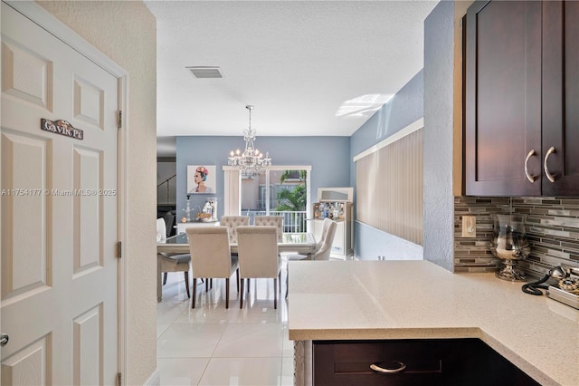 kitchen featuring light stone counters, visible vents, decorative backsplash, decorative light fixtures, and a chandelier