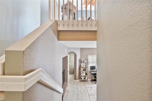 staircase featuring wood finished floors, a high ceiling, a textured wall, and arched walkways