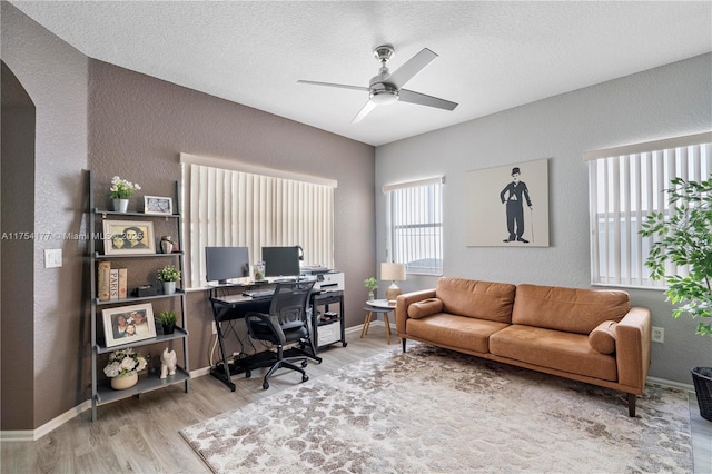 office featuring a textured wall, baseboards, a ceiling fan, and wood finished floors