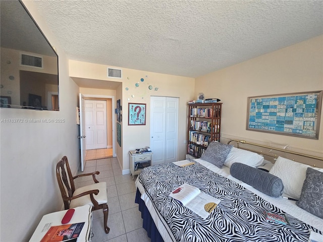 bedroom featuring light tile patterned floors, visible vents, a closet, and a textured ceiling