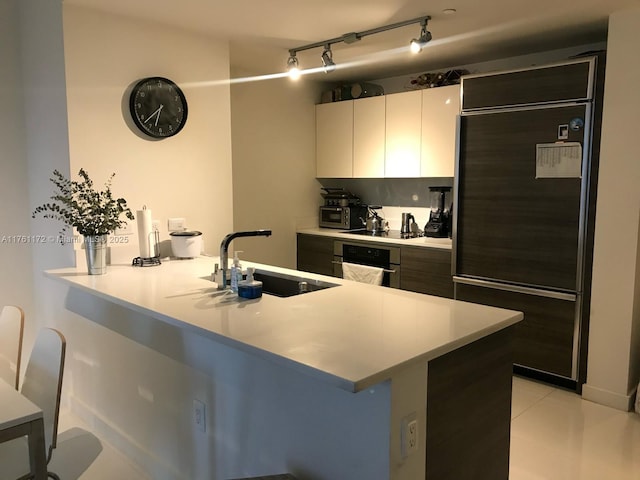 kitchen with a peninsula, oven, a sink, built in refrigerator, and a kitchen breakfast bar