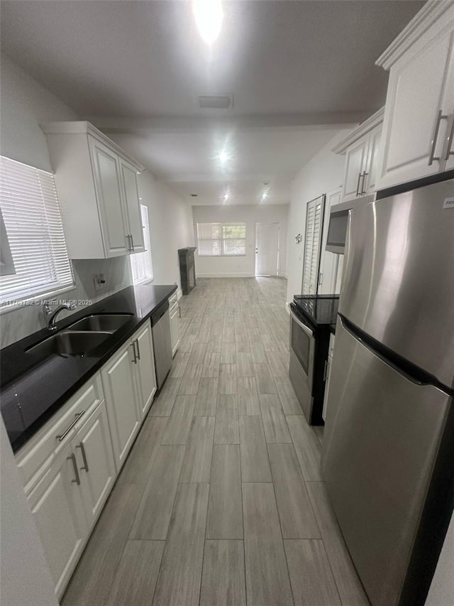 kitchen featuring wood finish floors, a sink, stainless steel appliances, white cabinetry, and dark countertops