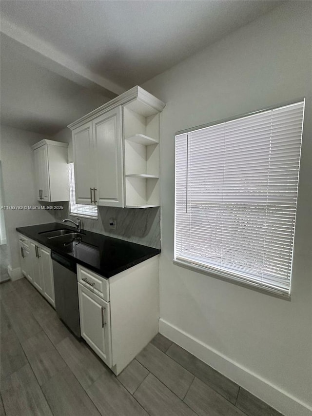 kitchen featuring stainless steel dishwasher, dark countertops, white cabinetry, and a sink