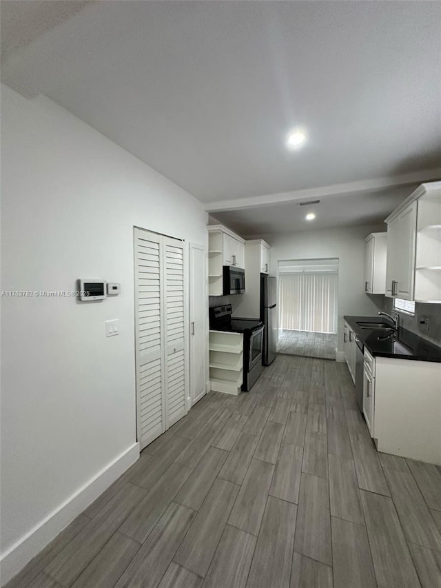 kitchen with open shelves, baseboards, white cabinets, stainless steel appliances, and a sink