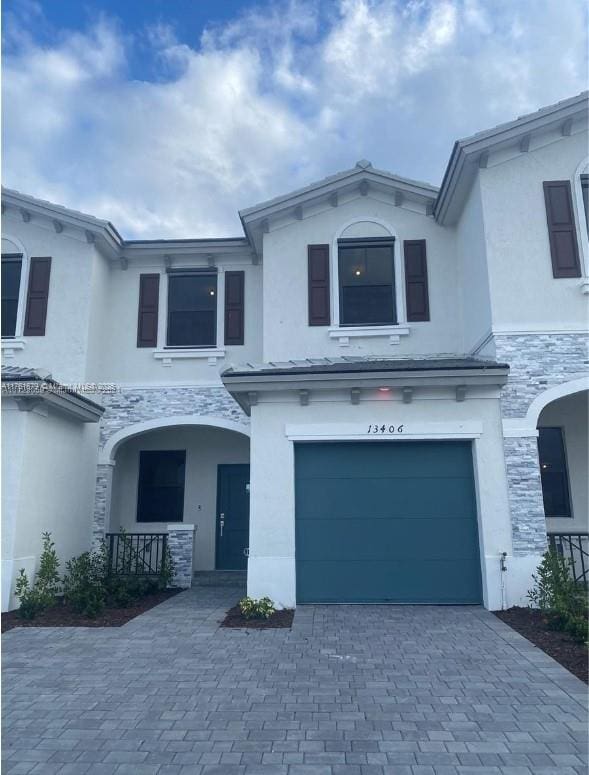 view of front of home with stucco siding, covered porch, a garage, stone siding, and driveway