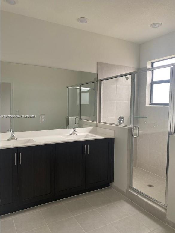 bathroom with tile patterned flooring, double vanity, a stall shower, and a sink