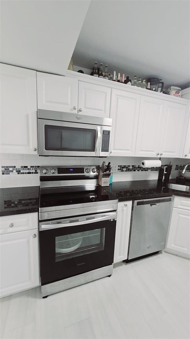 kitchen with a sink, decorative backsplash, appliances with stainless steel finishes, white cabinetry, and dark countertops