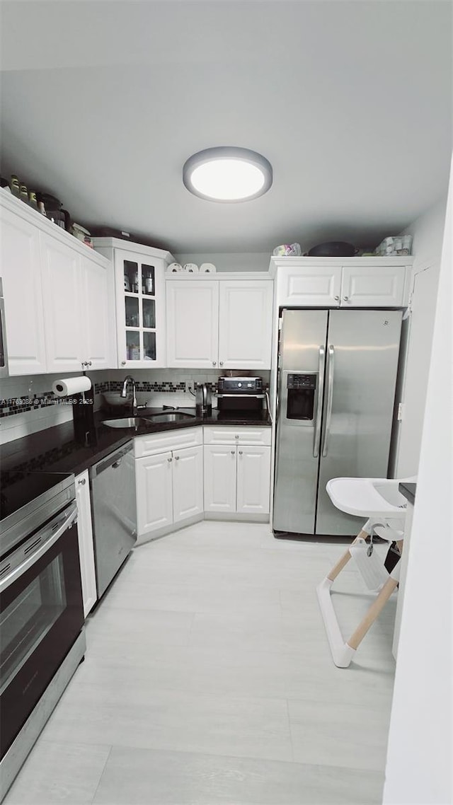 kitchen featuring dark countertops, glass insert cabinets, appliances with stainless steel finishes, white cabinets, and a sink