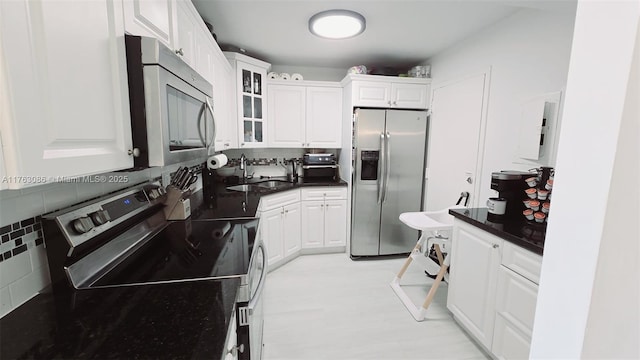 kitchen featuring a sink, white cabinets, glass insert cabinets, appliances with stainless steel finishes, and backsplash