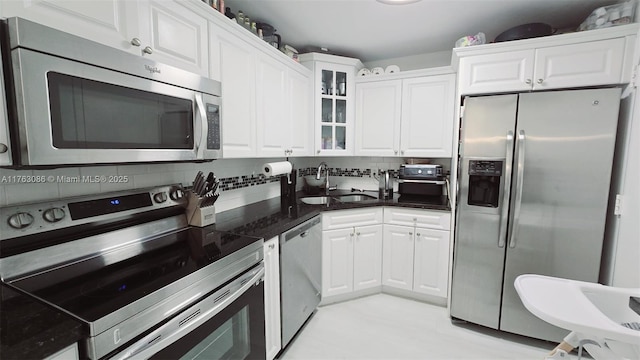 kitchen with a sink, backsplash, appliances with stainless steel finishes, white cabinets, and glass insert cabinets