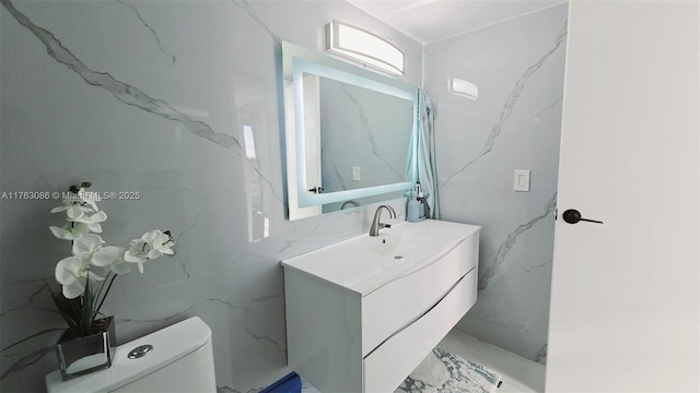 bathroom with vanity, stone wall, toilet, and marble finish floor