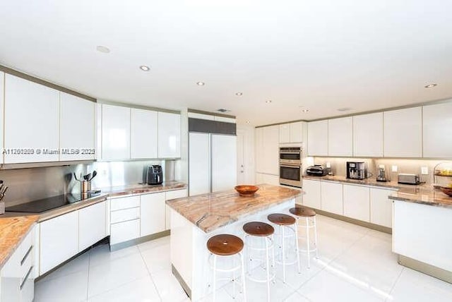 kitchen with stainless steel double oven, a kitchen breakfast bar, built in fridge, and white cabinets