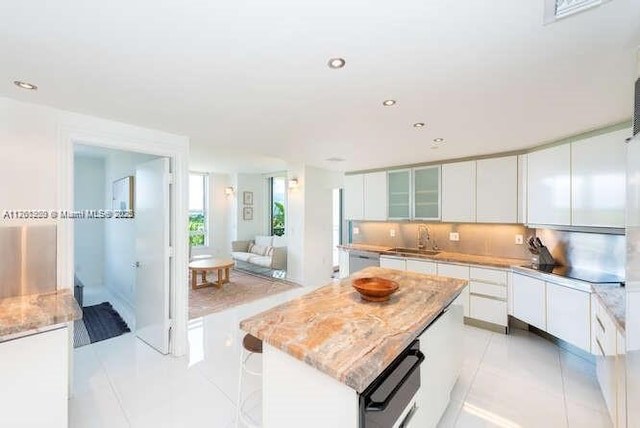 kitchen featuring a sink, white cabinetry, light tile patterned floors, decorative backsplash, and light stone countertops