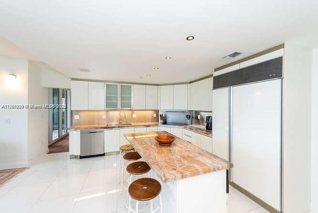 kitchen with backsplash, stainless steel dishwasher, white cabinets, white built in refrigerator, and light tile patterned floors