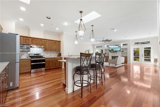 kitchen featuring a breakfast bar area, brown cabinetry, a skylight, stainless steel appliances, and under cabinet range hood