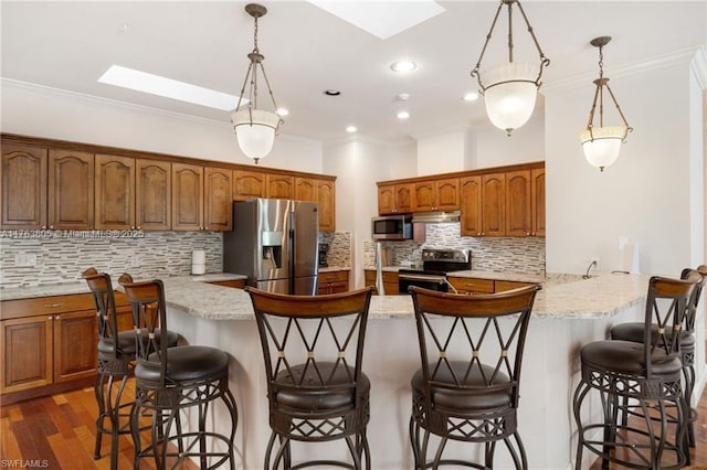 kitchen featuring under cabinet range hood, dark wood-style floors, a peninsula, appliances with stainless steel finishes, and a skylight