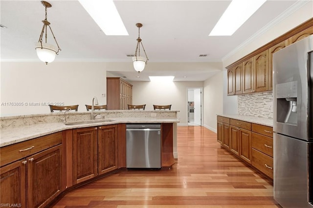 kitchen featuring light wood-style flooring, a sink, ornamental molding, stainless steel appliances, and pendant lighting