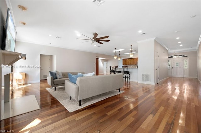 living room with visible vents, crown molding, a ceiling fan, and light wood finished floors