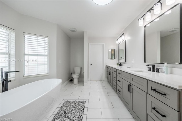 bathroom with visible vents, a freestanding tub, toilet, a sink, and double vanity