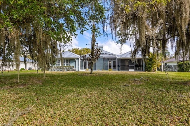 back of house with glass enclosure, a lawn, and metal roof