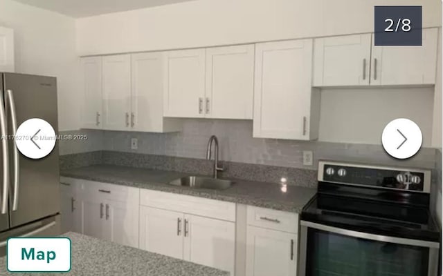 kitchen featuring a sink, tasteful backsplash, white cabinetry, appliances with stainless steel finishes, and light stone countertops