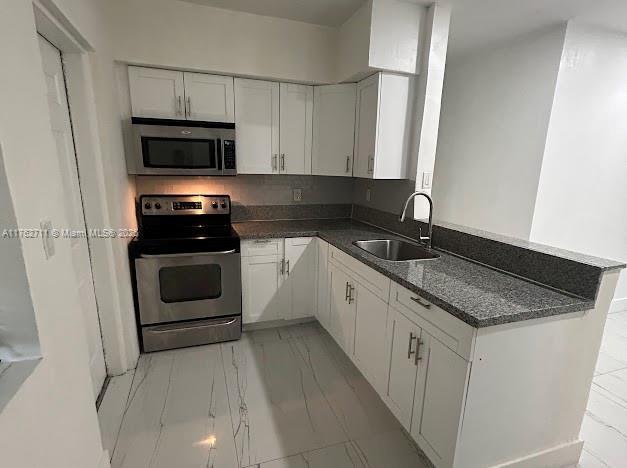 kitchen with marble finish floor, a sink, white cabinetry, appliances with stainless steel finishes, and a peninsula