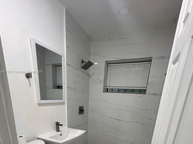 full bath featuring tiled shower and a sink