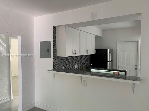 kitchen featuring tasteful backsplash, electric panel, a kitchen breakfast bar, freestanding refrigerator, and white cabinetry