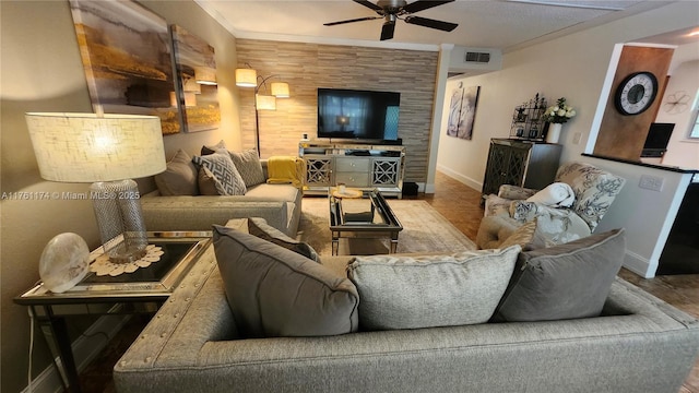 living area with visible vents, an accent wall, a ceiling fan, and ornamental molding