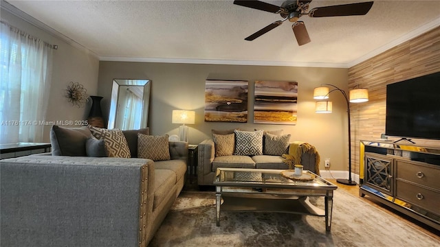 living area with wood finished floors, a ceiling fan, baseboards, a textured ceiling, and crown molding